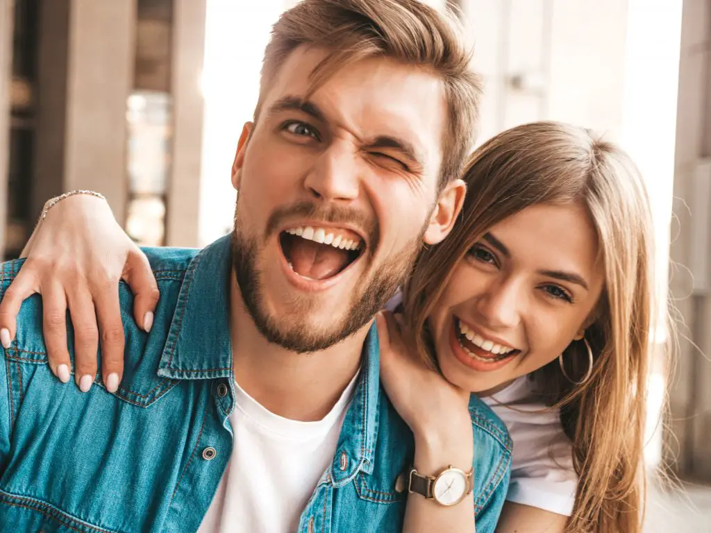 Portrait d'une belle fille souriante et de son beau petit ami. Femme en tenue d'été décontractée en jean. Famille heureuse et joyeuse. Femme s'amusant sur le fond de la rue. Clin d'œil