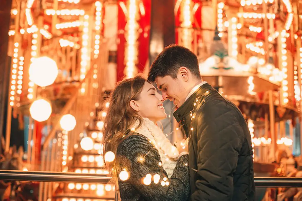 jeune couple qui s'embrasse à noel devant un manège